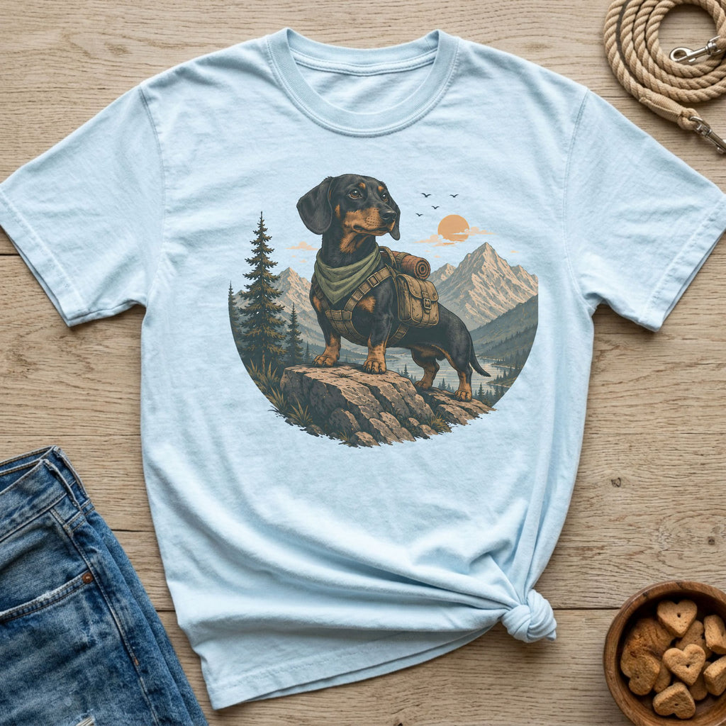 Light blue t-shirt with a graphic of a dachshund wearing a backpack on a mountain.