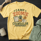 Yellow t-shirt with "Camp Zoomie Counselor" graphic, including a clipboard, paw print, and coffee mug.