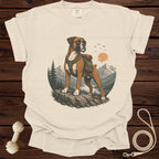 Boxer dog wearing a backpack on a rocky cliff overlooking a mountain lake at sunset.