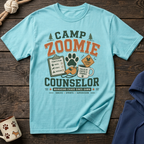 Light blue t-shirt with "Camp Zoomie Counselor" graphic, including a checklist, whistle, and coffee mug.
