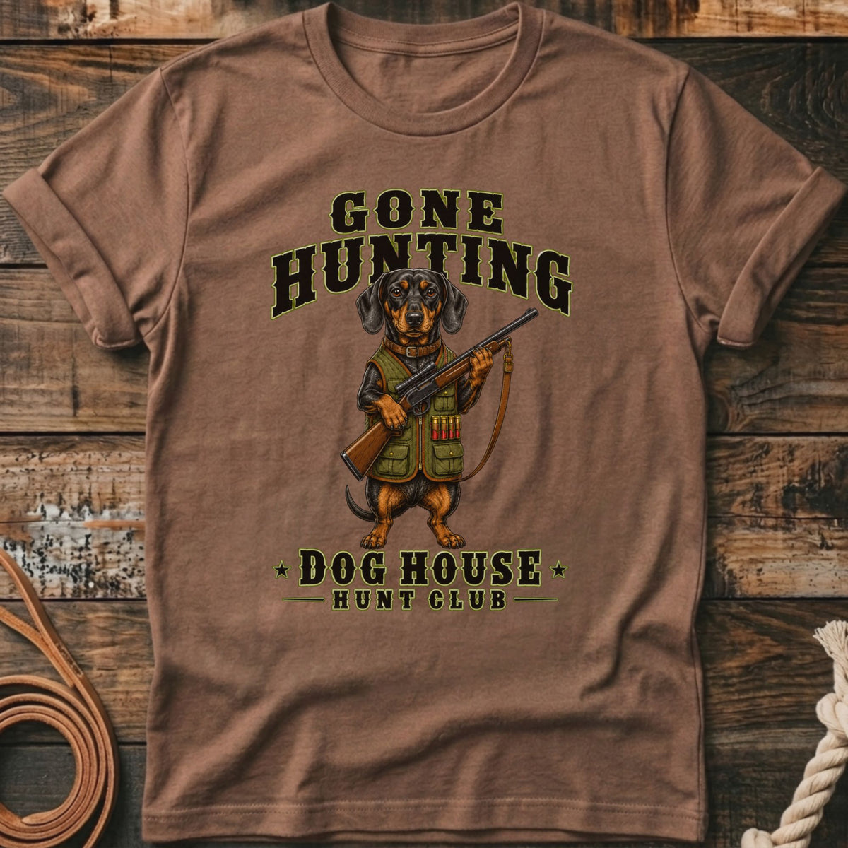 T-shirt graphic of a dachshund in hunting gear holding a rifle, with text "Gone Hunting" and "Dog House Hunt Club."