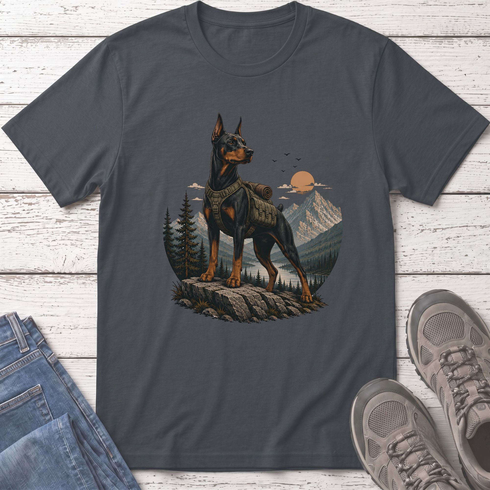 Doberman with backpack on rock overlooking lake and mountains at sunset.