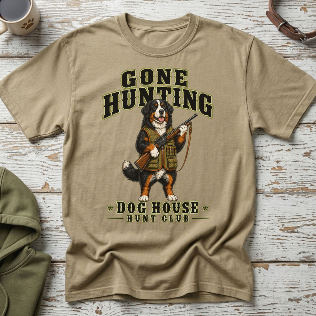 Bernese Mountain Dog wearing hunting vest holds a rifle with "Gone Hunting Dog House Hunt Club" text.