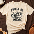 Cream t-shirt with black text "I WORK HARD SO MY DOG CAN IGNORE ME IN COMFORT CLUB ZOOMIE".
