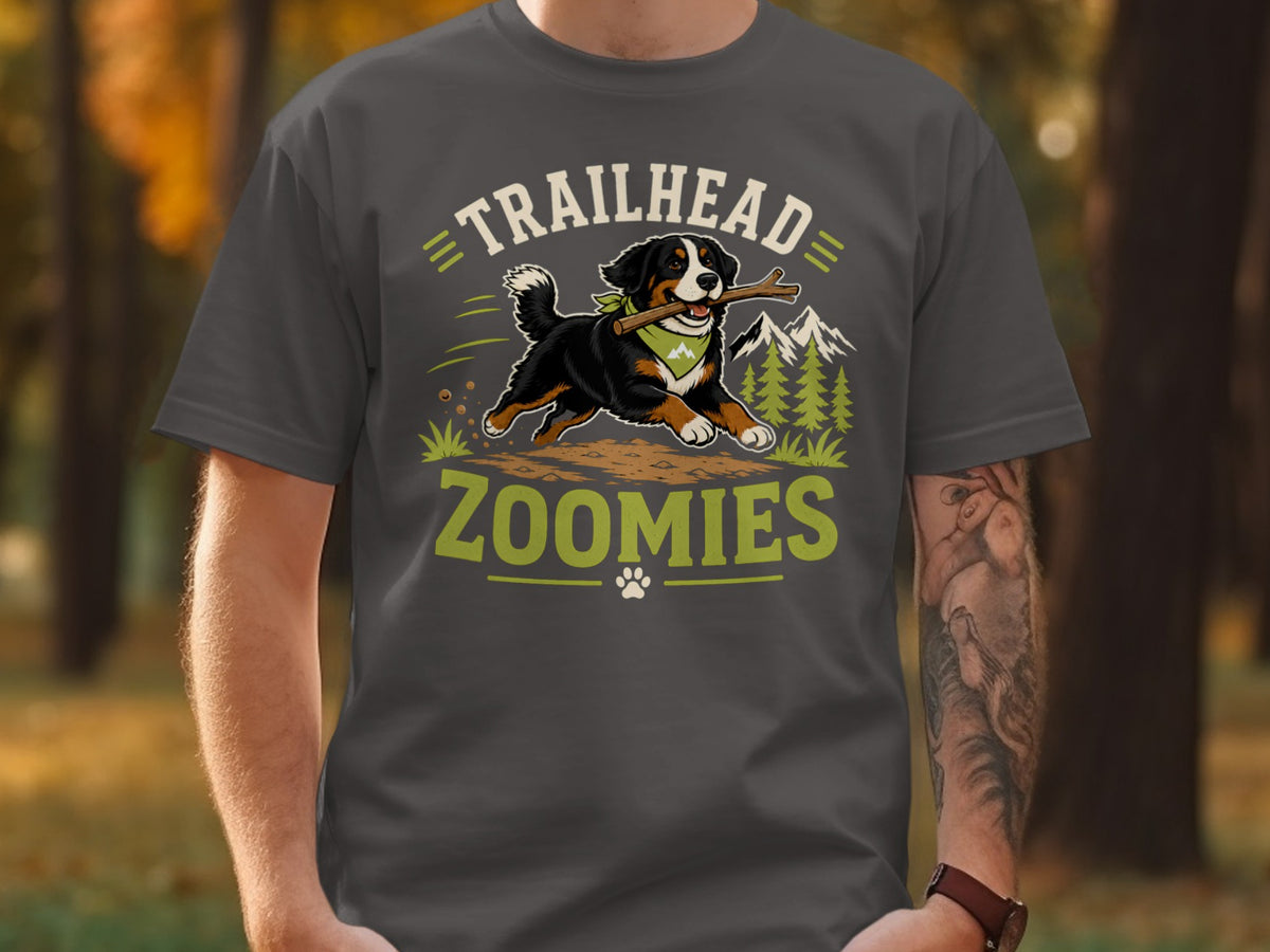 Bernese Mountain Dog with stick, "TRAILHEAD ZOOMIES" text, trees, and mountains graphic on shirt.