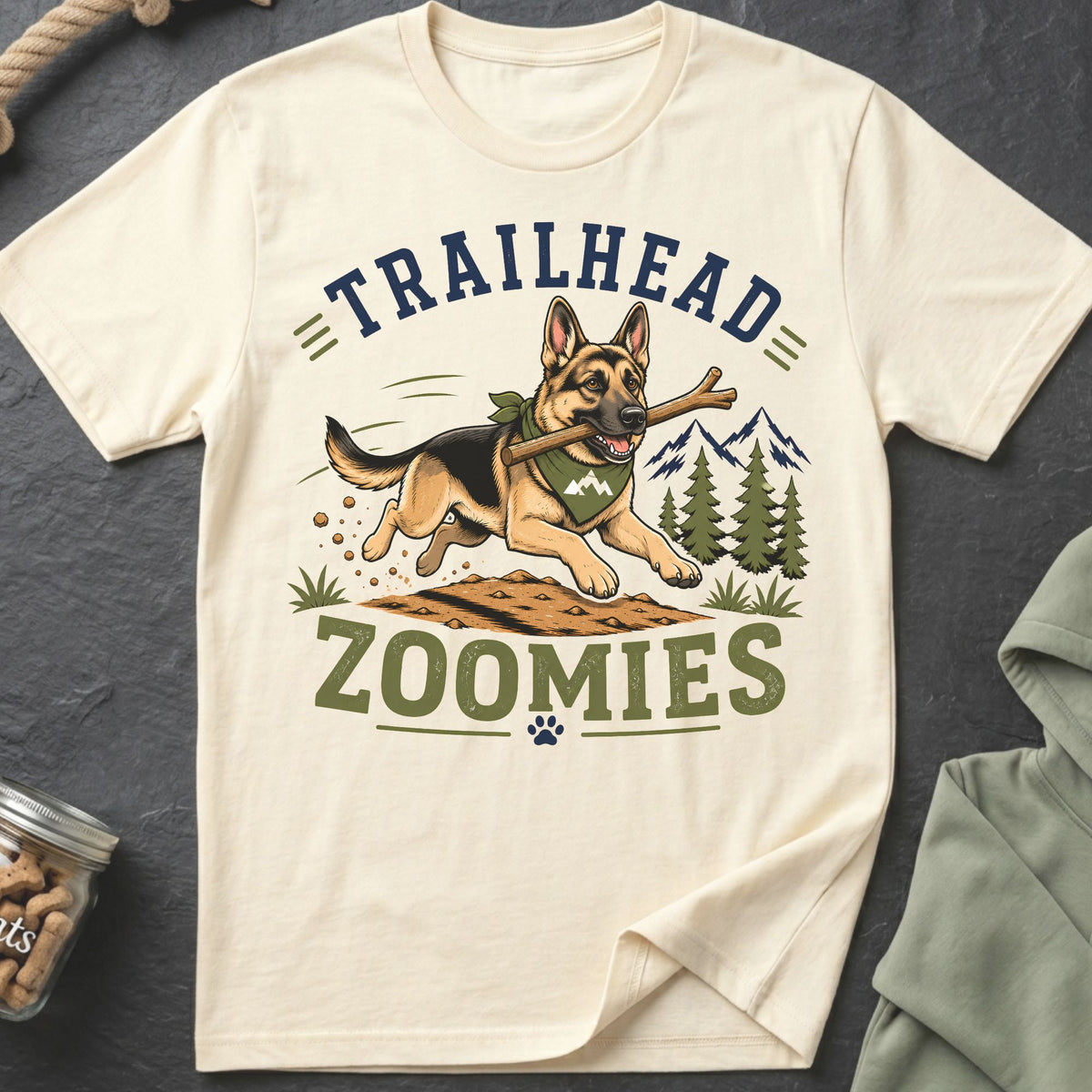 German Shepherd with stick and bandana, "TRAILHEAD ZOOMIES" text, mountains, and trees.