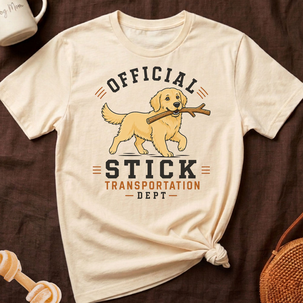 Cream t-shirt with a golden retriever carrying a stick, text reads "OFFICIAL STICK TRANSPORTATION DEPT".
