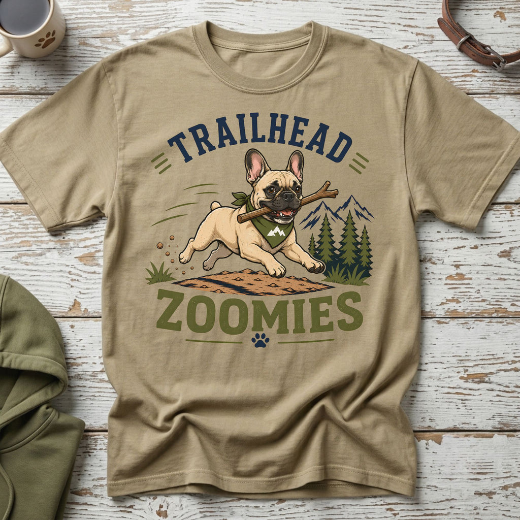 French bulldog running with stick, "TRAILHEAD ZOOMIES" text, pine trees, and mountains.