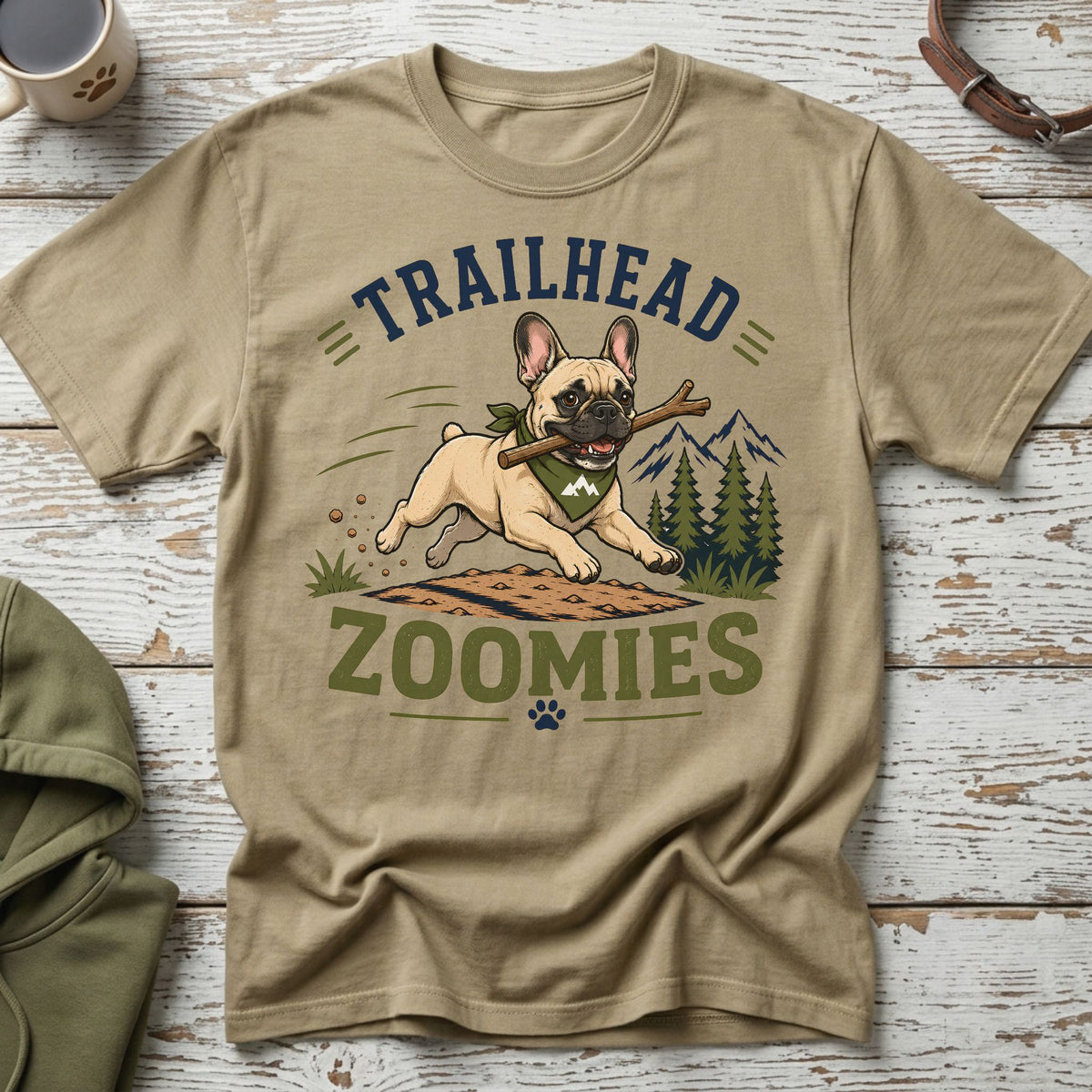French bulldog running with stick, "TRAILHEAD ZOOMIES" text, pine trees, and mountains.