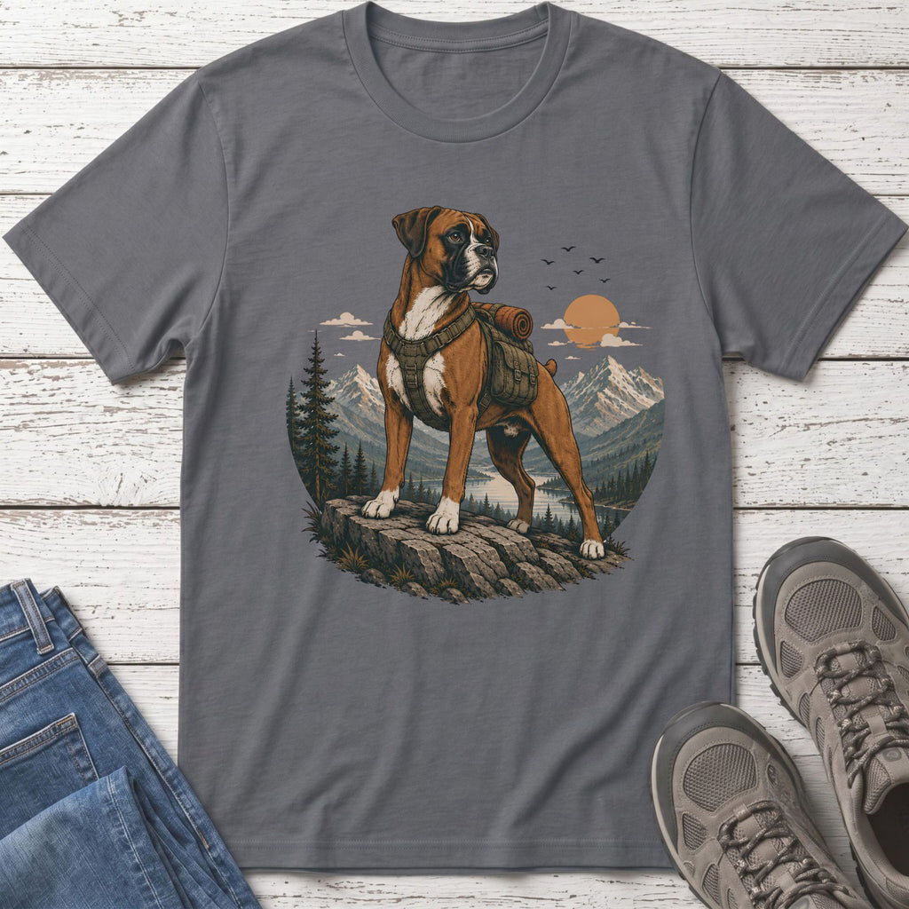 Boxer dog wearing a backpack stands on rock overlooking a mountain lake at sunset.