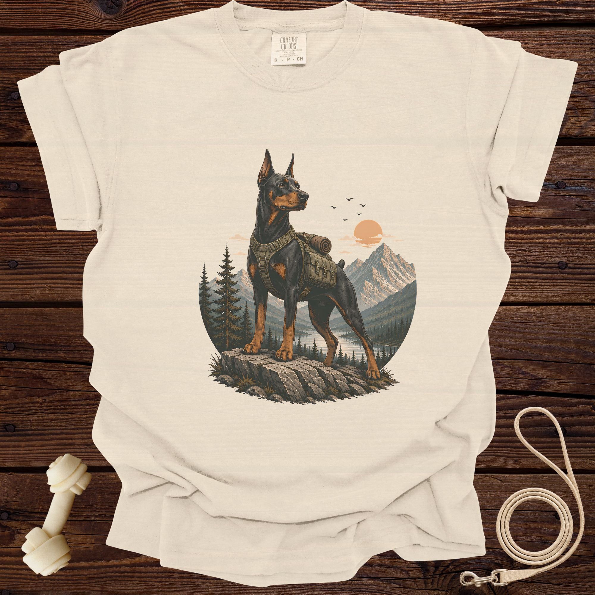 Cream t-shirt with a Doberman wearing a backpack in a mountain landscape graphic.