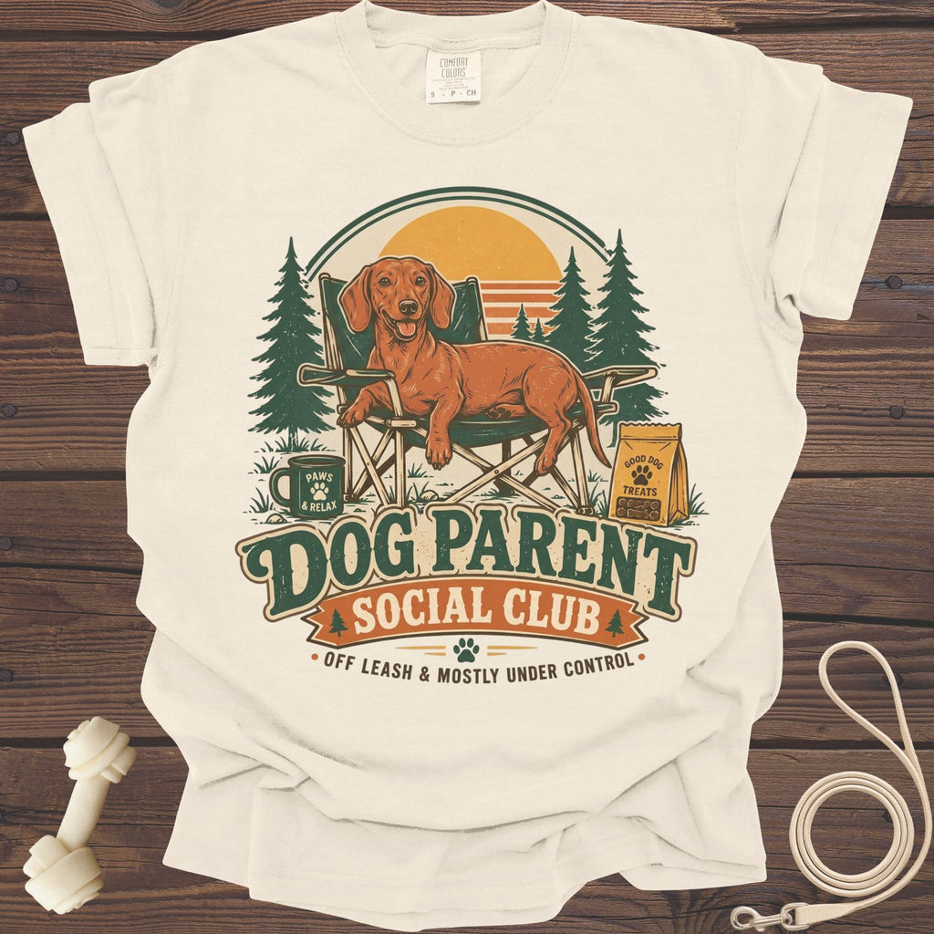 Cream t-shirt with a dachshund in a camping chair, text "Dog Parent Social Club."