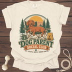 Cream t-shirt with a dachshund in a camping chair, text "Dog Parent Social Club."