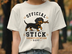 White t-shirt graphic with dachshund carrying a stick, "OFFICIAL STICK TRANSPORTATION DEPT" text.
