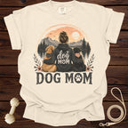 Dog Mom graphic on cream t-shirt with two dogs, mountains, and sunset scene.