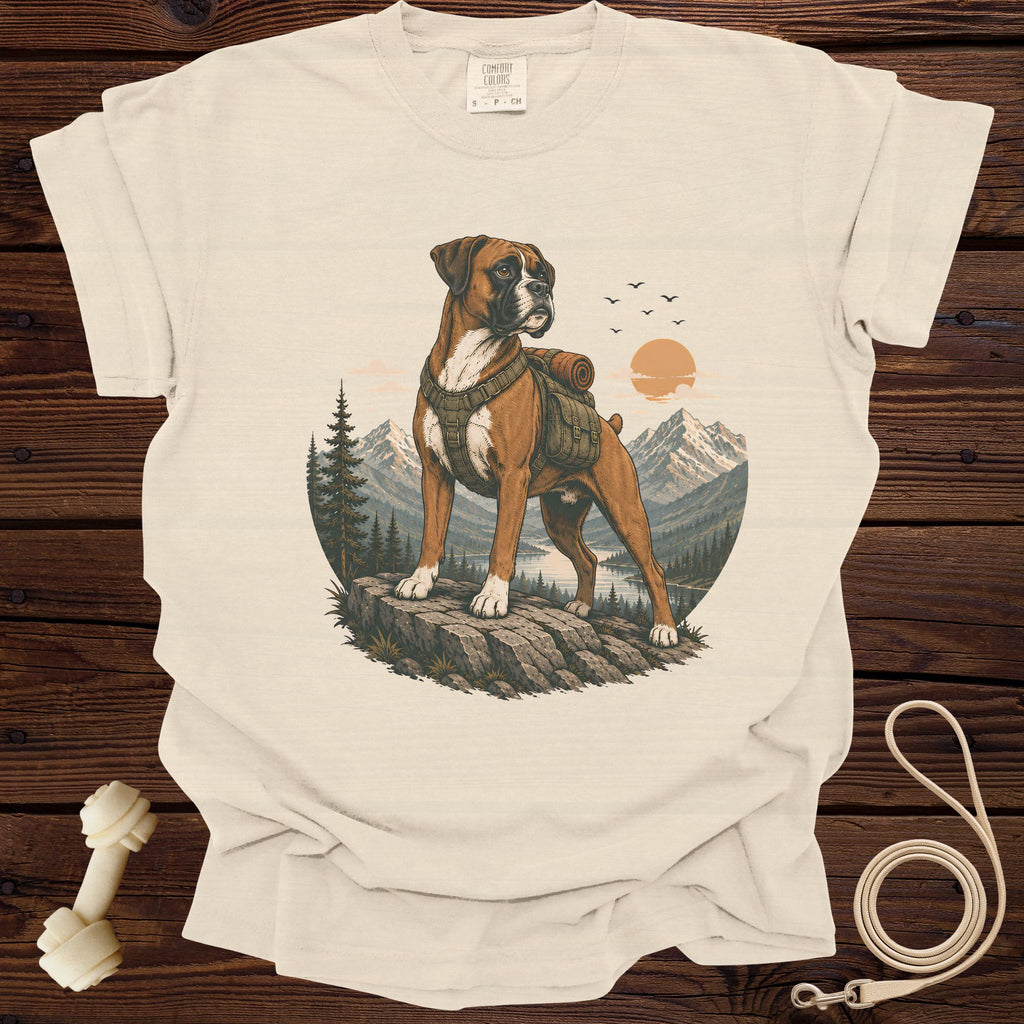 Boxer dog with backpack on rock, overlooking mountains, lake, and sunset scene.