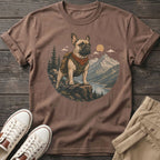 French bulldog wearing backpack and bandana on rocky outcrop overlooking mountains and lake.
