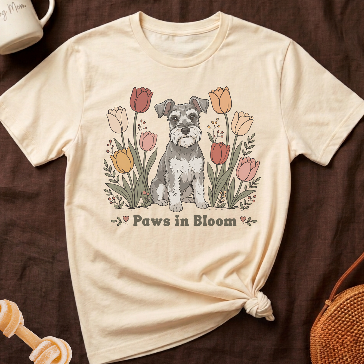 Cream t-shirt with a schnauzer in front of blooming tulips and text "Paws in Bloom".