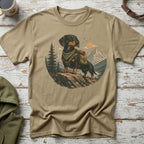T-shirt graphic of a dachshund wearing a backpack and scarf on a rocky outcrop with mountains.