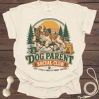 A dog relaxes in a chair with text "Dog Parent Social Club" and trees.