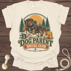Rottweiler in a chair with "Dog Parent Social Club" text and outdoor scene.