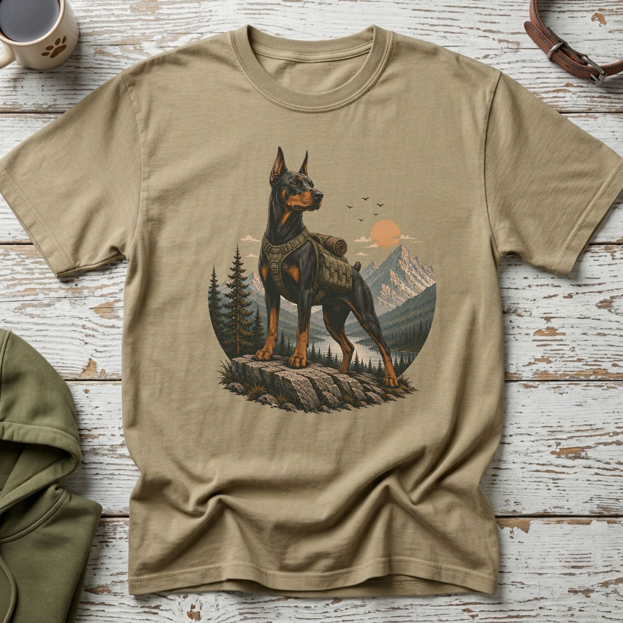 Doberman wearing a backpack stands on rocks with mountains and sunset behind.