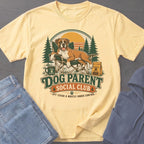 Light yellow t-shirt graphic with boxer dog, text "Dog Parent Social Club", and outdoor scene.