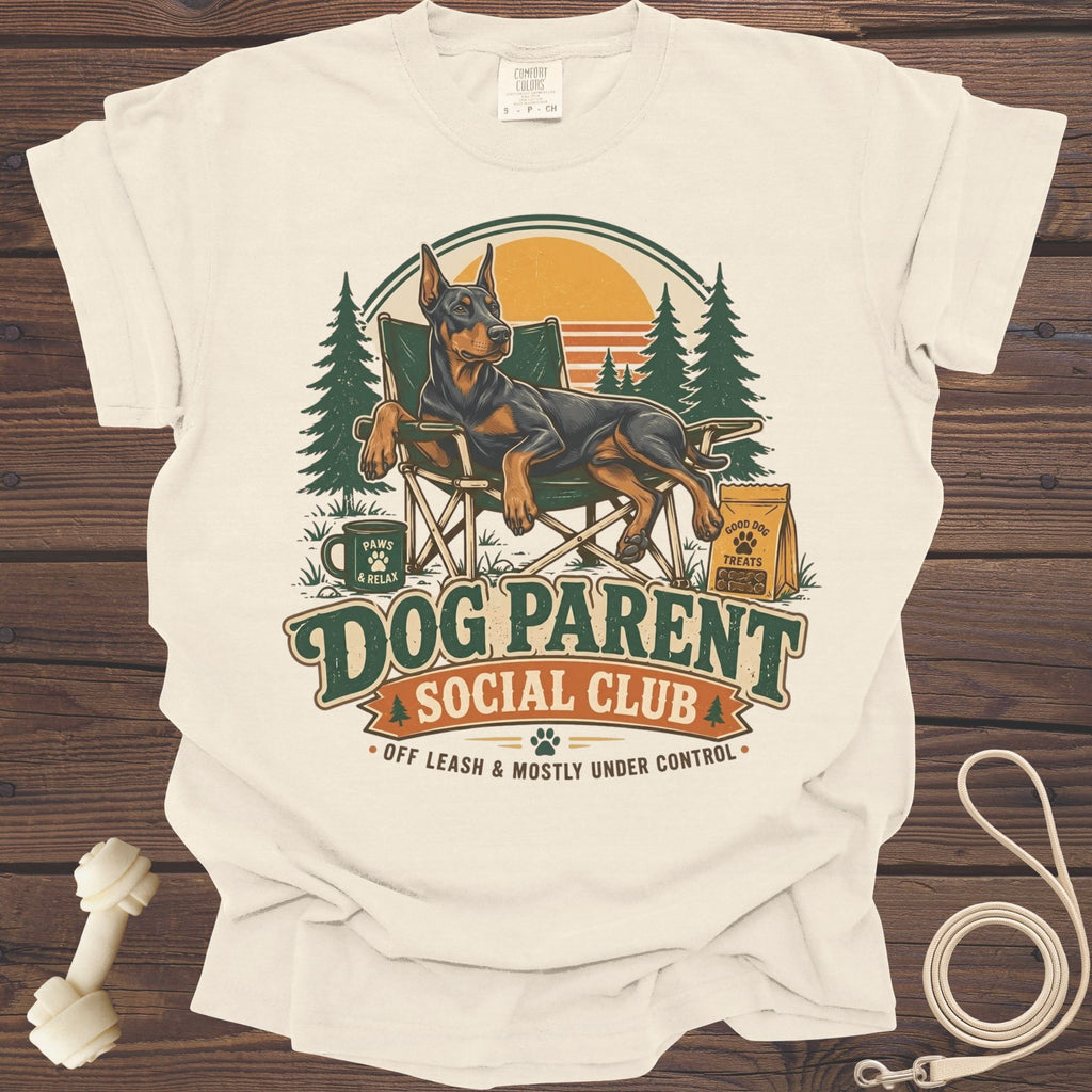 Cream t-shirt with Doberman relaxing in a chair, "Dog Parent Social Club" text.