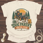 Cream t-shirt with Doberman relaxing in a chair, "Dog Parent Social Club" text.