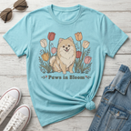 Light blue t-shirt with a fluffy dog sitting amongst cartoon tulips and the text "Paws in Bloom".