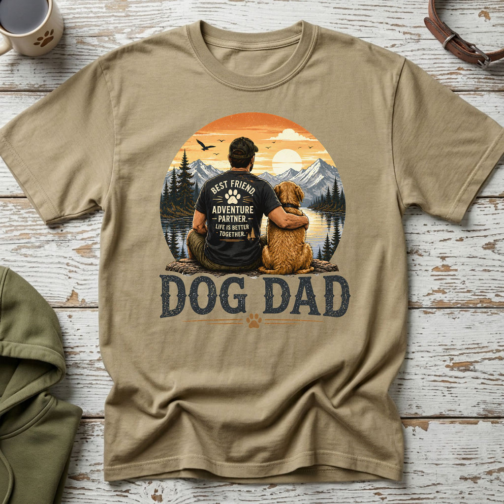 Tan t-shirt with "DOG DAD" and a man hugging his dog in a scenic mountain sunset.