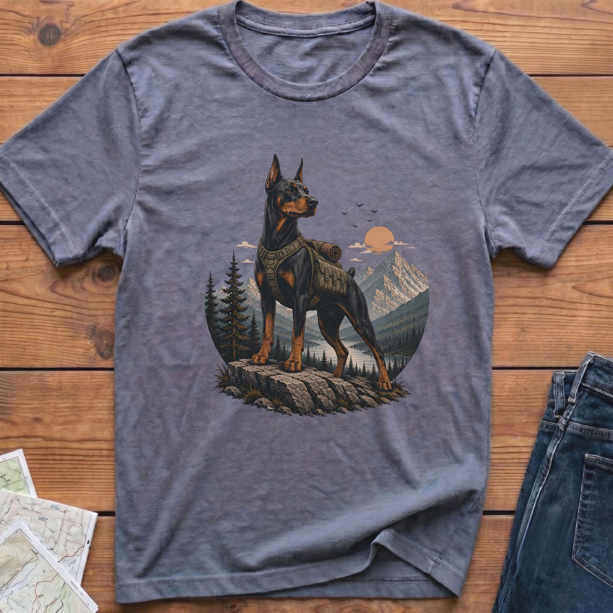 Doberman on a rock with backpack, facing mountains at sunset.