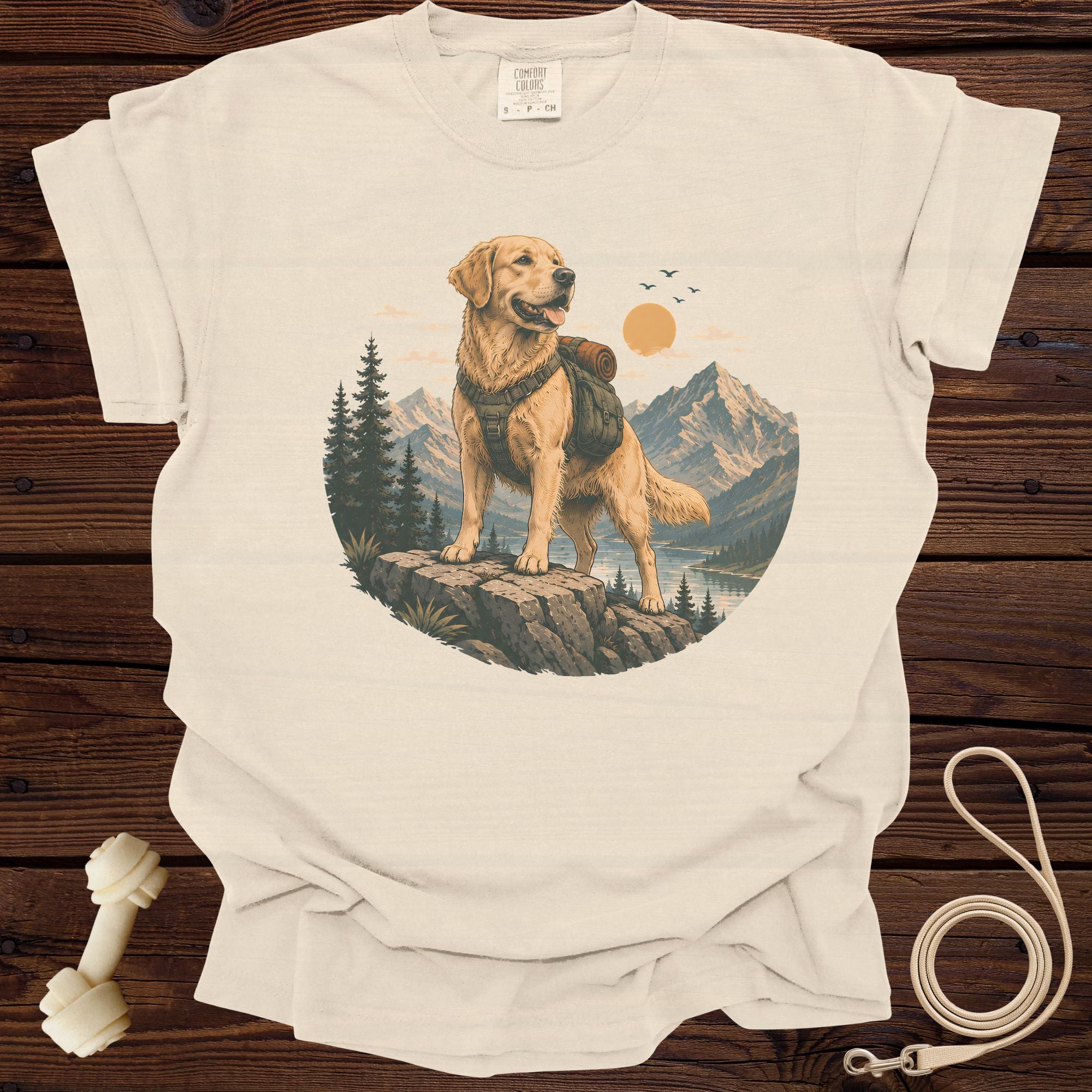 Golden retriever wearing backpack stands on rock with mountain and lake background.