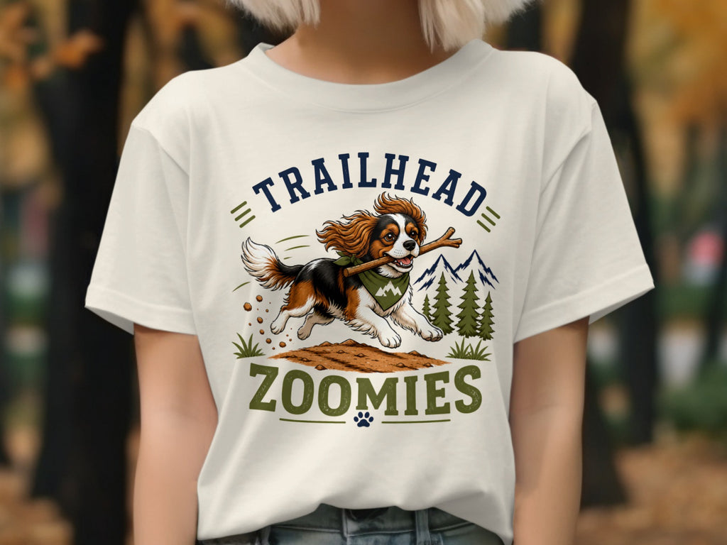 Tricolor dog with stick runs with text "TRAILHEAD ZOOMIES" on t-shirt.