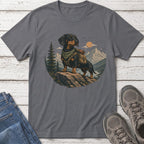 Dachshund in hiking gear stands on a rock overlooking a mountainous landscape.
