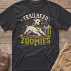 White dog with bandana runs with stick, "Trailhead Zoomies" text, mountains.