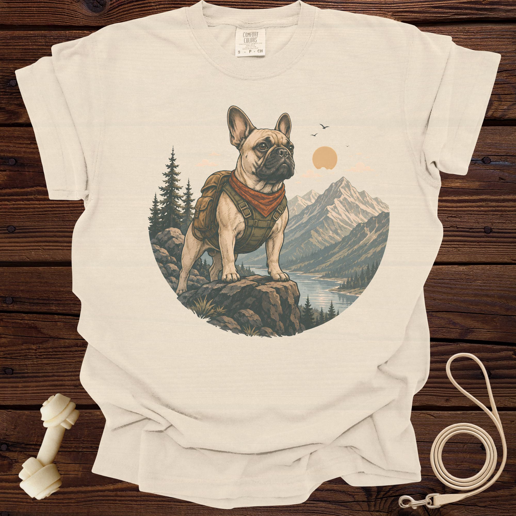 French bulldog wearing backpack and bandana on mountain overlook with lake and sun.