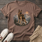 German Shepherd wearing a backpack stands on a rock with mountain scenery.