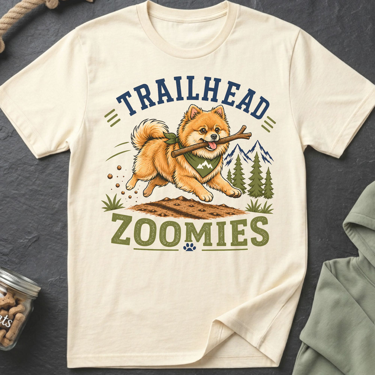 Cream t-shirt with a graphic of a happy Pomeranian running with a stick, text "TRAILHEAD ZOOMIES".