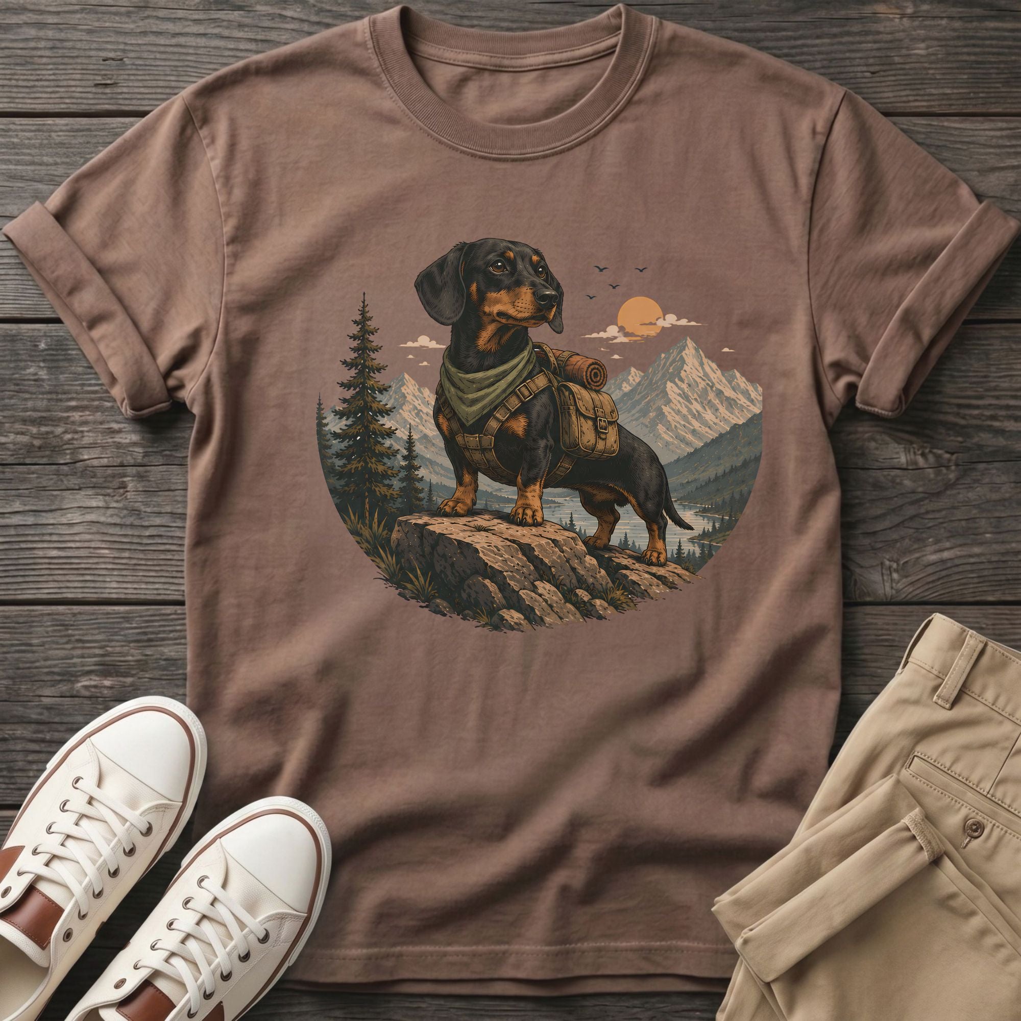 Dachshund wearing backpack stands on rock with mountain and lake backdrop.