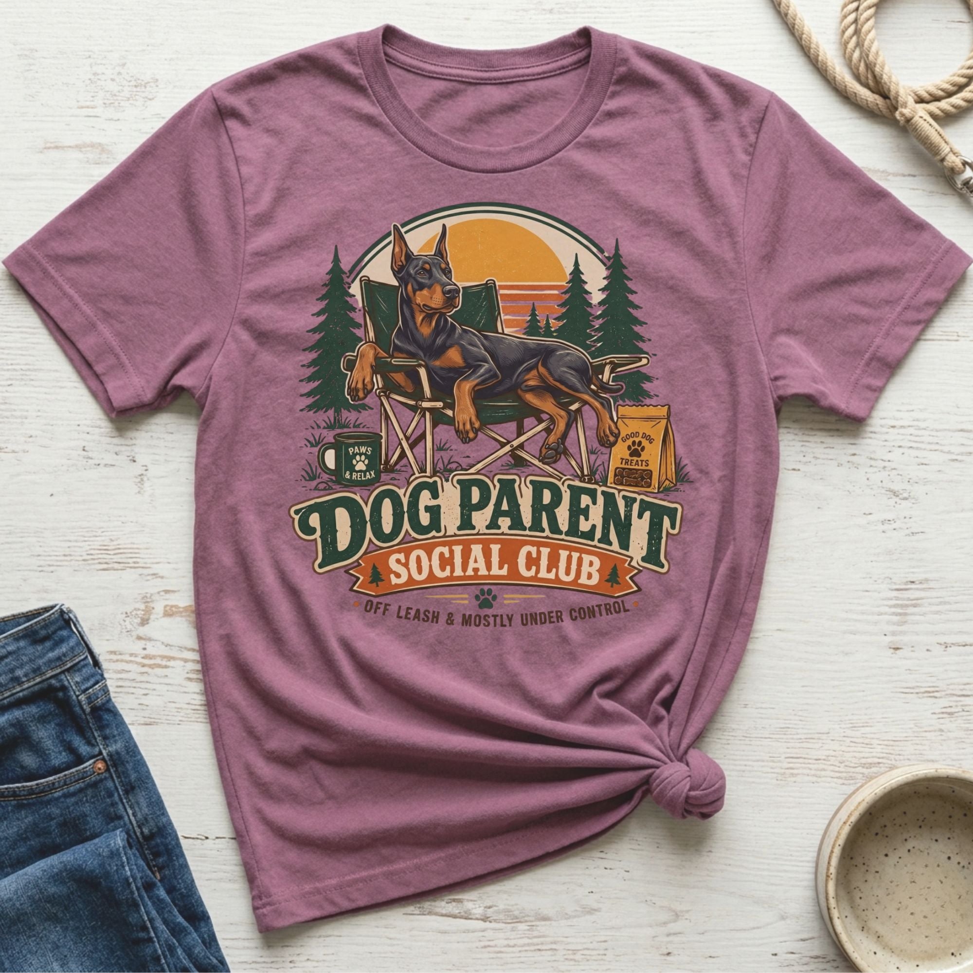 Doberman relaxes in a camping scene with text "Dog Parent Social Club".