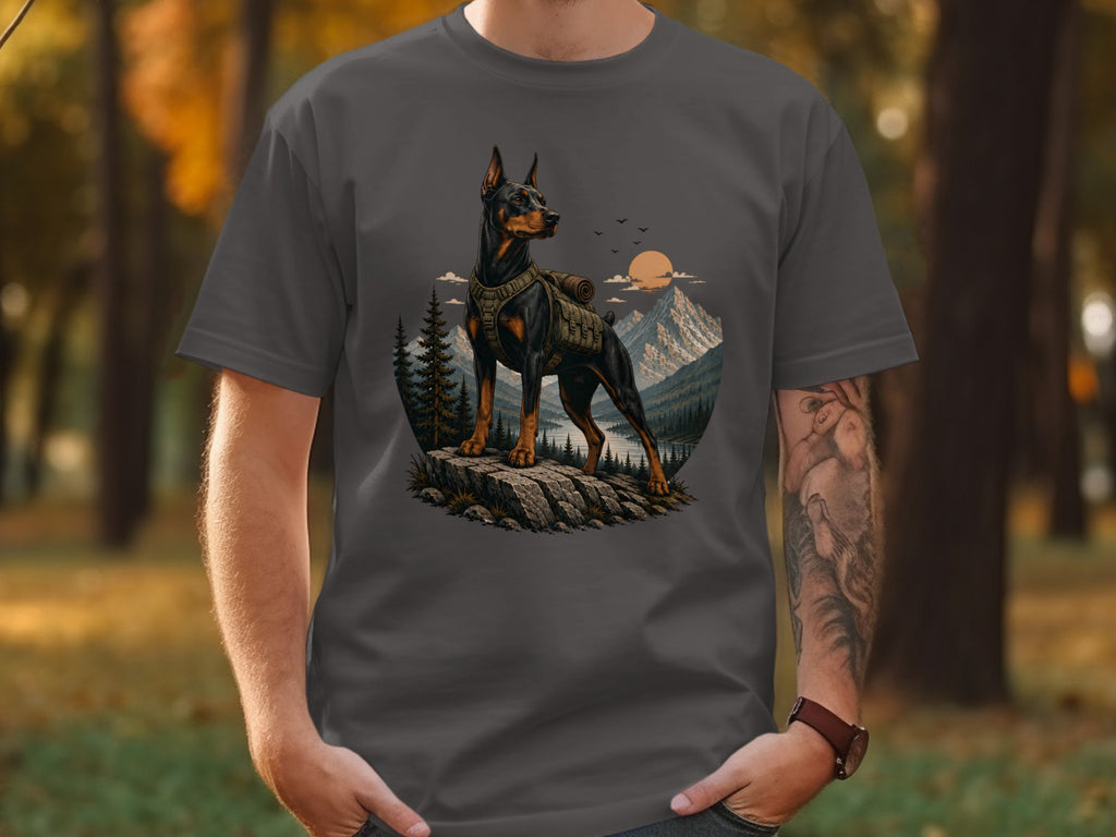 Doberman with backpack stands on rocks, mountains, lake, and trees behind.